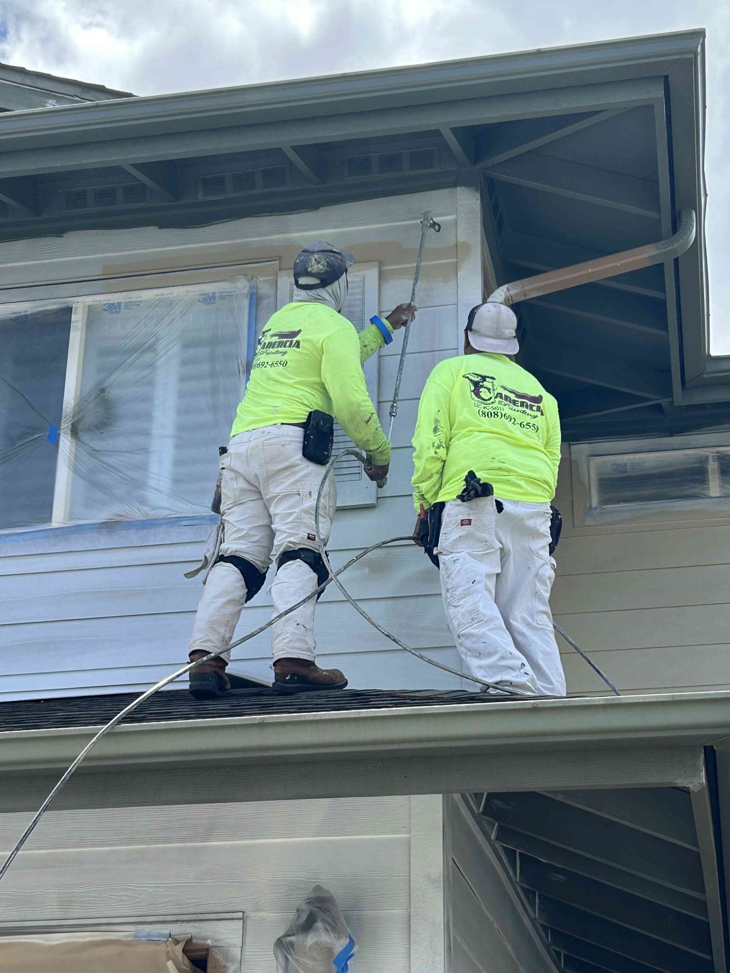 Canencia crew in neon yellow shirts painting the exterior of an Oahu home